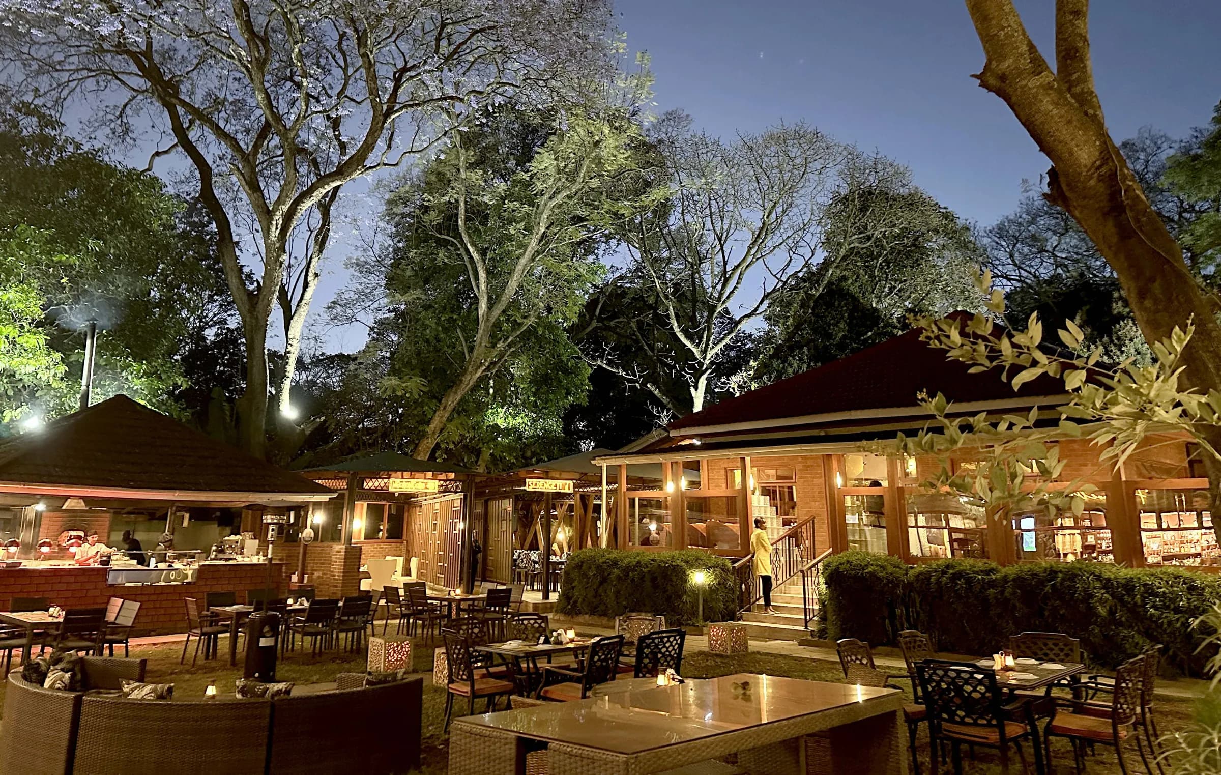Amber's garden at dusk: thatched pavilions glowing with warm light beneath tall trees